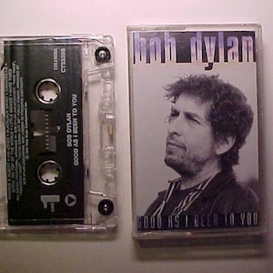 May include: A cassette tape and a compact disc case with a photo of Bob Dylan on the front. The text on the case reads "Good as I Been to You" and "Bob Dylan".