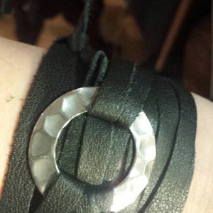 May include: Black leather wrap bracelet with a hammered silver-tone metal ring. The bracelet wraps around the wrist multiple times. The leather has a textured appearance.