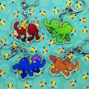 May include: Four colorful cartoon character keychains with silver key rings. The characters are a red and yellow monster, a green monster with a trunk, a blue monster with three eyes, and an orange monster with a long tail.