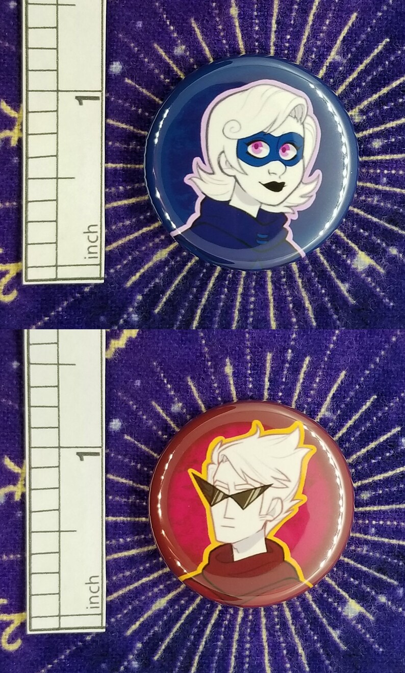 Puede incluir: Dos pines de bot&oacute;n de 2,5 cm que representan personajes de dibujos animados con cabello blanco. El primer pin tiene un fondo azul y presenta un personaje con una m&aacute;scara morada. El segundo pin tiene un fondo rojo y presenta un personaje con gafas de sol.