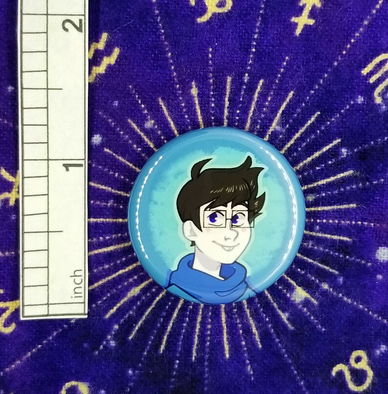 Puede incluir: Un bot&oacute;n azul y blanco con una ilustraci&oacute;n de dibujos animados de una persona con cabello casta&ntilde;o que lleva gafas y un su&eacute;ter azul.