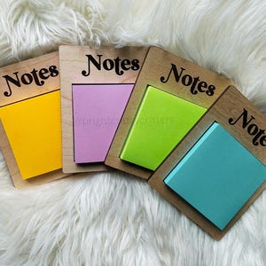 May include: Four wooden note holders with the word "Notes" written on each. Each holder has a different coloured sticky note attached: yellow, pink, green, and blue.