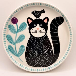 May include: A white ceramic mug with a black handle and the text "But First, Coffee" in a black, bold font. The mug is on a wooden surface. The mug is 10 cm tall.
