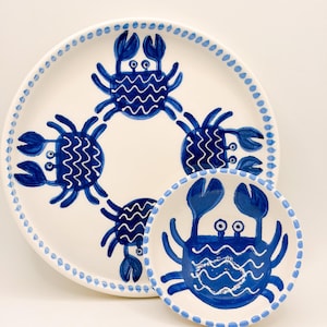 May include: White ceramic serving plate and small bowl with a blue crab design. The plate features four crabs in a circle, and the bowl has one crab. Both have a dotted blue border.