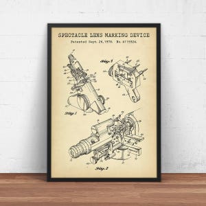 以下が含まれることがあります： 眼鏡レンズマーキング装置のヴィンテージな白黒の特許図面。図面は、さまざまな部品にラベル付けされ、番号が付けられた装置の詳細なイラストを示しています。特許は1978年9月26日に出願され、特許番号は4115924です。
