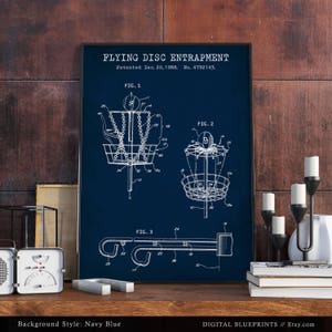Może przedstawiać: Drukowany plakat w kolorze granatowym z vintage'owym rysunkiem patentowym urządzenia do łapania latającego dysku. Patent nosi tytuł "Flying Disc Entrapment" i został opatentowany 20 grudnia 1988 roku. Numer patentu to 4792143. Rysunek przedstawia trzy r&oacute;żne widoki urządzenia. Plakat jest idealny dla entuzjasty frisbee.