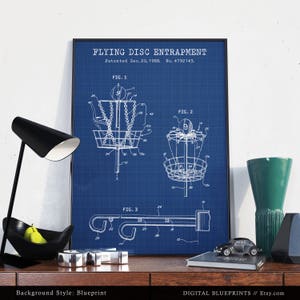 Może przedstawiać: Ilustracja w stylu planu technicznego patentu na urządzenie do chwytania latającego dysku. Patent został opatentowany 20 grudnia 1988 roku, a jego numer to 4792143. Ilustracja przedstawia trzy r&oacute;żne widoki urządzenia, kt&oacute;re jest rodzajem kosza do frisbee.