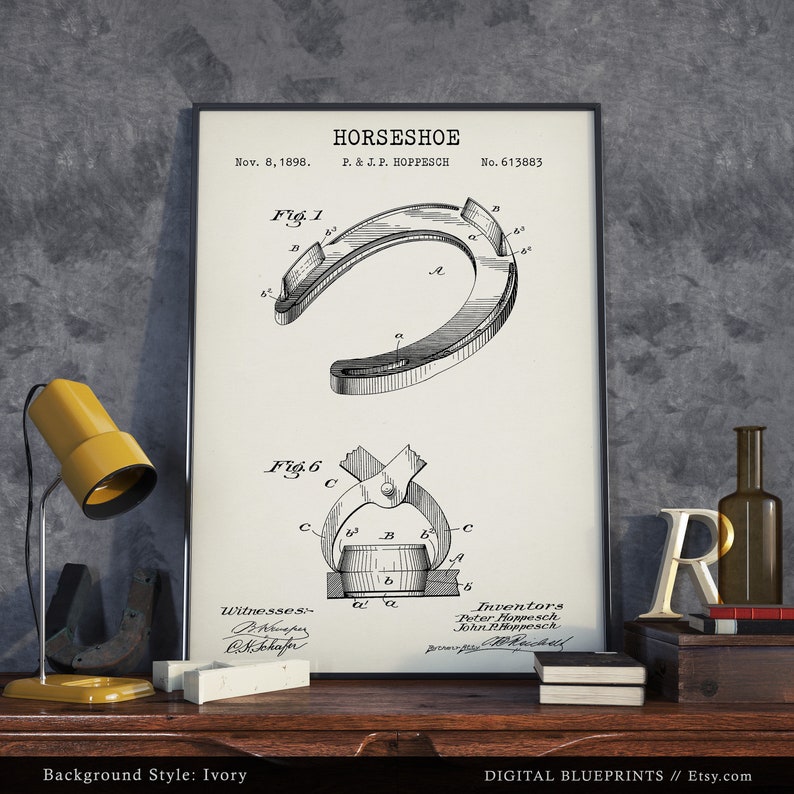 May include: A black and white patent drawing of a horseshoe design. The drawing shows the horseshoe in detail, with labels and numbers indicating different parts of the horseshoe. The patent information is included at the top of the drawing, including the date, inventor's name, and patent number. The drawing is framed and displayed on a wooden surface with a lamp and other decorative items.