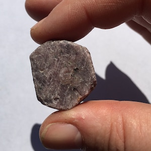 以下が含まれることがあります： わずかに不規則な形をした、ざらざらとした濃い紫色の宝石。宝石はざらざらとした質感のある表面を持ち、自然な研磨されていない石です。