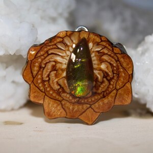 May include: A teardrop-shaped iridescent opal gemstone set in a wooden pendant with a carved floral design.