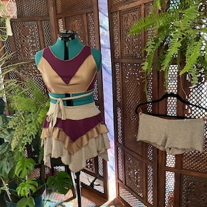 May include: A two-piece outfit with a gold and burgundy top and a grey skirt with gold and burgundy accents. The skirt has a ruffled hem.