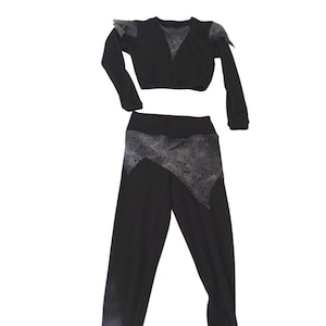 Puede incluir: Un conjunto de baile negro con un top corto de manga larga y leggings. El top tiene una superposición de encaje en los hombros y un ribete de encaje alrededor de la cintura. Los leggings tienen una superposición de encaje en la parte delantera.