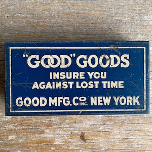 May include: A rectangular, vintage blue metal sign with white lettering. The sign reads "GOOD' GOODS" at the top, followed by "INSURE YOU AGAINST LOST TIME" and "GOOD MFG. CO. NEW YORK" at the bottom. The sign has a distressed appearance.