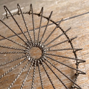May include: A vintage wire whisk with a circular shape and a central hole. The whisk is made of twisted wire and has a silver finish.