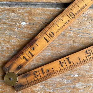 May include: A folding wooden ruler made of boxwood with a brass hinge. The ruler features black printed imperial measurements and the text "WARRANTED BOXWOOD" visible on the surface. The wood has a natural light brown grain and aged patina.