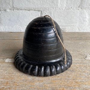 May include: Black cast iron beehive shaped bell with a string attached. The bell has a ribbed design and a scalloped edge.