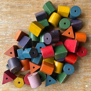 May include: A selection of brightly coloured wooden blocks in diverse shapes, such as cylinders, triangles, and hexagons. The blocks are painted in red, green, yellow, blue, and orange. Each block has a hole drilled through the centre.