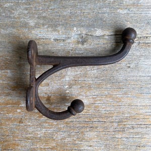 May include: A rustic, cast iron hook with a rounded top and a decorative scroll design. The hook is dark brown with a weathered finish.