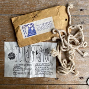 May include: A vintage magic trick set with a beige rope, a brown paper envelope, and a printed instruction sheet. The envelope has a blue and white label reading "Simplex Cut & Restored Rope Trick". The instruction sheet shows diagrams.