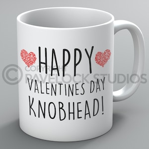 Peut inclure: Une tasse en céramique blanche avec un motif noir et rouge. La tasse dit "Happy Valentines Day Knobhead!" avec deux cœurs rouges de chaque côté du mot "Happy".