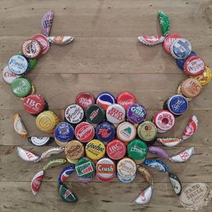 Puede incluir: Un cangrejo colorido hecho de tapas de botellas sobre un fondo de madera. El cangrejo está hecho de una variedad de tapas de botellas de diferentes colores, incluyendo rojo, azul, verde, amarillo y naranja. Las tapas de botellas están dispuestas en un patrón que se asemeja al cuerpo y las patas de un cangrejo. El cangrejo está sentado sobre un fondo de madera, que está pintado en un color marrón claro. El fondo está hecho de tablones de madera. El cangrejo es un símbolo popular de la playa y el océano.