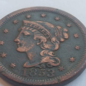 May include: A copper-colored US one-cent coin with a portrait of Liberty and the date 1853.