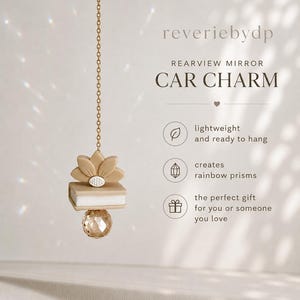 Puede incluir: Un adorno para espejo retrovisor con cadena dorada, flor de loto beige, elemento en forma de libro blanco y esfera de cristal facetado. El texto incluye reveriebydp, REARVIEW MIRROR CAR CHARM, lightweight and ready to hang, creates rainbow prisms y the perfect gift for you or someone you love.