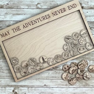 May include: A wooden display board with the engraved text "MAY THE ADVENTURES NEVER END". The board holds several small, round wooden tokens, each etched with a different state or landmark design. The tokens are scattered around the board.
