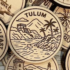 May include: Wooden coaster featuring a Tulum, Mexico design. The coaster has a circular shape with a detailed illustration of a coastal landscape, including a pyramid, palm trees, and the word "TULUM" in a bold font. The design is etched in dark brown.