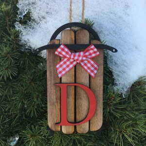 May include: Wooden sled Christmas ornament with a red and white gingham bow and the letter "D" painted in red.
