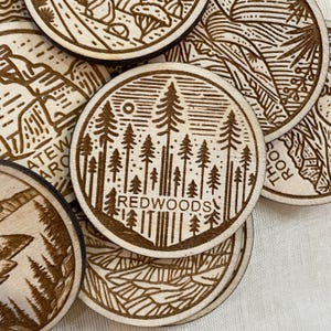 May include: A set of round wooden coasters with laser-etched designs of trees and the words "REDWOODS" on one coaster.