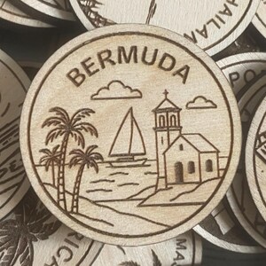 May include: A round wooden souvenir featuring a laser-etched design of Bermuda. The design includes palm trees, a sailboat, a church, and the word "BERMUDA" in a circular border. The wood has a light, natural color.