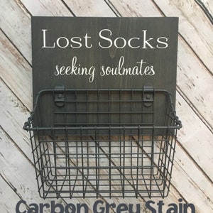 May include: A black wire basket with a wooden sign that reads "Lost Socks seeking soulmates" in white lettering. The sign is stained a dark grey color.