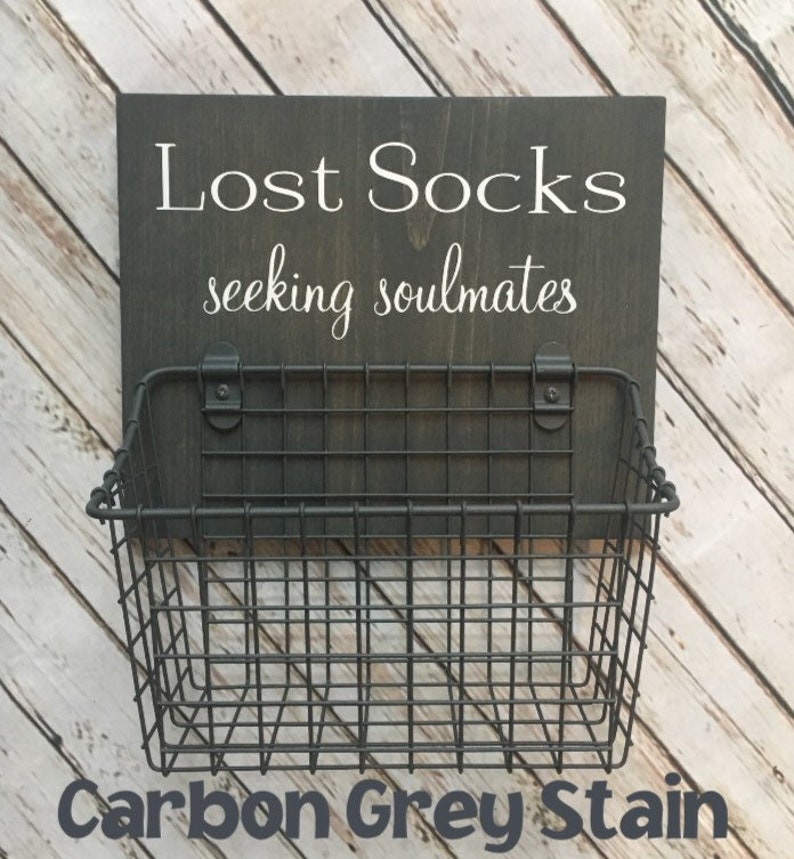 May include: A black wire basket with a wooden sign that reads "Lost Socks seeking soulmates" in white lettering. The sign is stained a dark grey color.