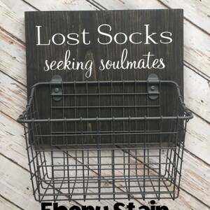 May include: A black wooden sign with the text "Lost Socks seeking soulmates" and a black wire basket attached below. The sign is stained with ebony stain.