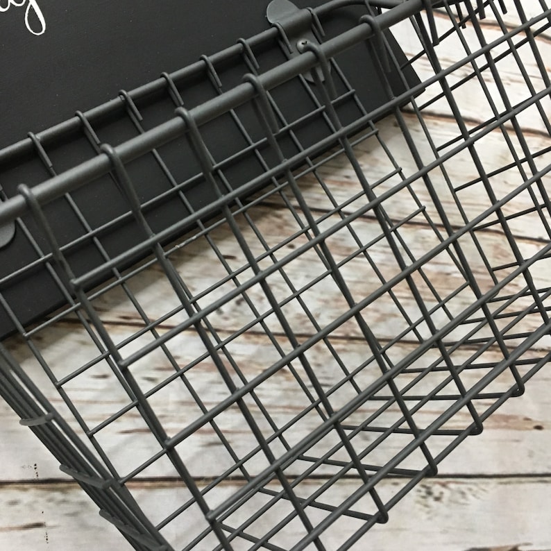 May include: A black metal wire basket with a rectangular shape. The basket is hanging from a wall and has a simple design.