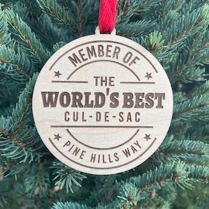 May include: A wooden Christmas ornament with the text "* MEMBER OF THE WORLD'S BEST CUL-DE-SAC ★ PINE HILLS WAY ★" on it.