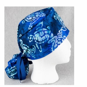 May include: Blue surgical scrub hat with a tie at the back. The hat has a white and blue batik pattern of sea turtles.