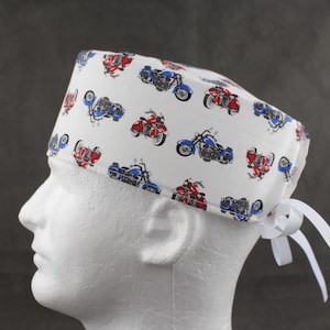 May include: White scrub hat with a pattern of red and blue motorcycles. The hat has white ties that can be tied at the back of the head.