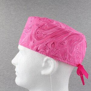 May include: Pink surgical scrub hat with a marbled pattern. The hat has a tie at the back.