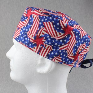 May include: A blue, red, and white surgical scrub hat with a pattern of American flags and stars.