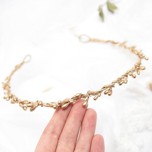 Puede incluir: Una diadema de metal dorado con un delicado diseño de hojas. La diadema está hecha de alambre fino y tiene pequeñas hojas redondeadas que están espaciadas uniformemente a lo largo de la banda.