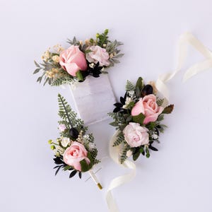 May include: Three pink rose buttonholes with greenery and black berries. The buttonholes are tied with white satin ribbon.