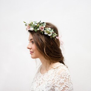 May include: A woman with long brown hair wearing a white lace dress and a floral crown with pink and white flowers.