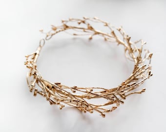 May include: A gold-colored twig crown or wreath made of thin, delicate branches. The crown is circular and has a simple, elegant design.