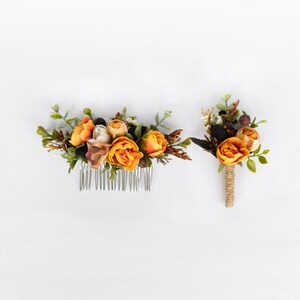 May include: A set of two floral hair accessories featuring orange and white flowers with brown accents. One piece is a comb and the other is a boutonniere.