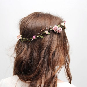 May include: A floral crown with pink roses and green leaves. The crown is worn on a person's head.