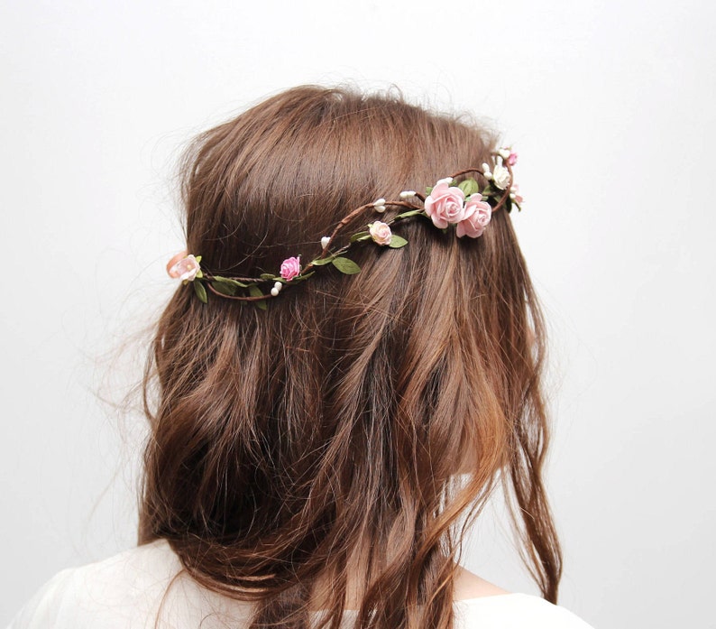 May include: A floral crown with pink roses and green leaves. The crown is worn on a person's head.