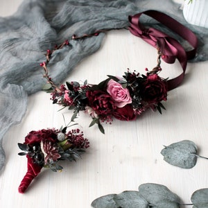 May include: A burgundy floral crown with a pink rose and a matching burgundy floral buttonhole.