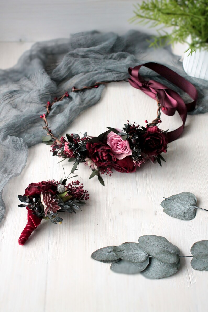 May include: A burgundy floral crown with a pink rose and a matching burgundy floral buttonhole.